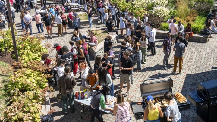 Dans la cour intérieure du cégep, on voit une foule de gens, à la fois des étudiants et des membres du personnel, qui viennent prendre des hot-dogs, qui discutent ou prennent le soleil, dans une ambiance de rentrée scolaire et de retrouvailles avec des amis.