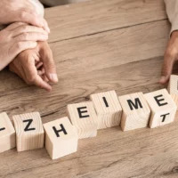 Des mains placent des cubes où apparaissent les lettres du mot Alzheimer