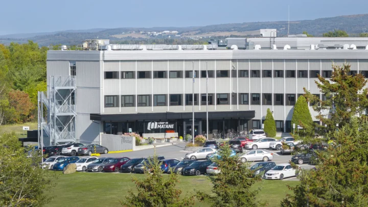 Une photo aérienne prise au drone du Cégep de Matane, notamment du stationnement et de l'entrée principale de l'établissement, avec des cimes d'arbres au premier plan.