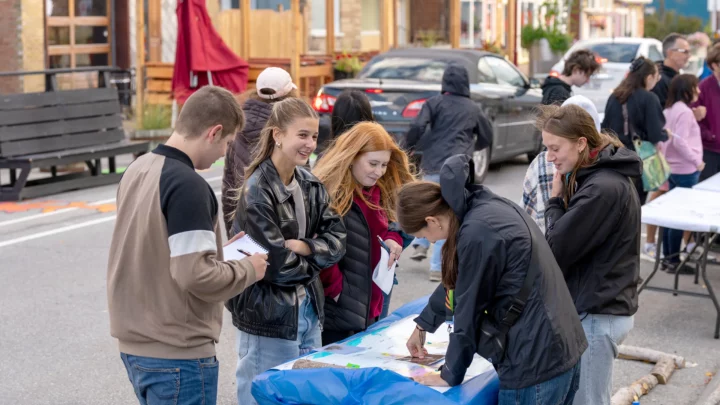 Des étudiantes et étudiants animent des kiosques interactifs au centre-ville de Matane dans le cadre du Park(ing) Day et discutent avec des gens qui viennent voir leur installation citoyenne.