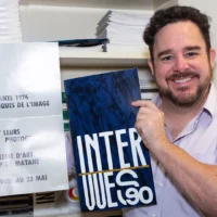 L'enseignant de photographie Maxence Bradley prend la pose avec deux catalogues de cohortes précédentes du programme.